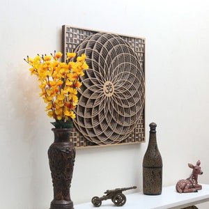 May include: A wooden wall art piece with a geometric design featuring a circular mandala with the symbol "Om" in the center. The mandala is surrounded by a square frame with a checkered pattern. The art piece is brown and has a natural wood finish.
