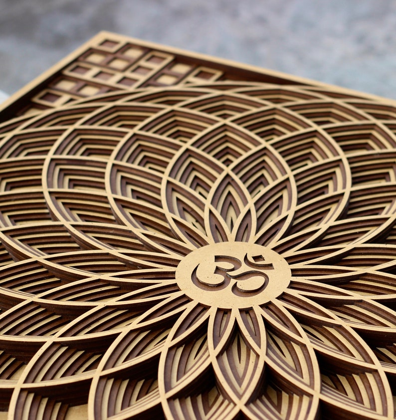 May include: A wooden wall art piece with a layered design of a flower with an Om symbol in the center. The flower is made of multiple layers of wood, creating a 3D effect.