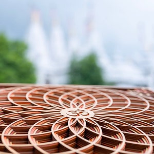 May include: A wooden mandala with a layered design featuring the Om symbol in the center. The mandala is made of multiple shades of brown wood and has a circular shape.