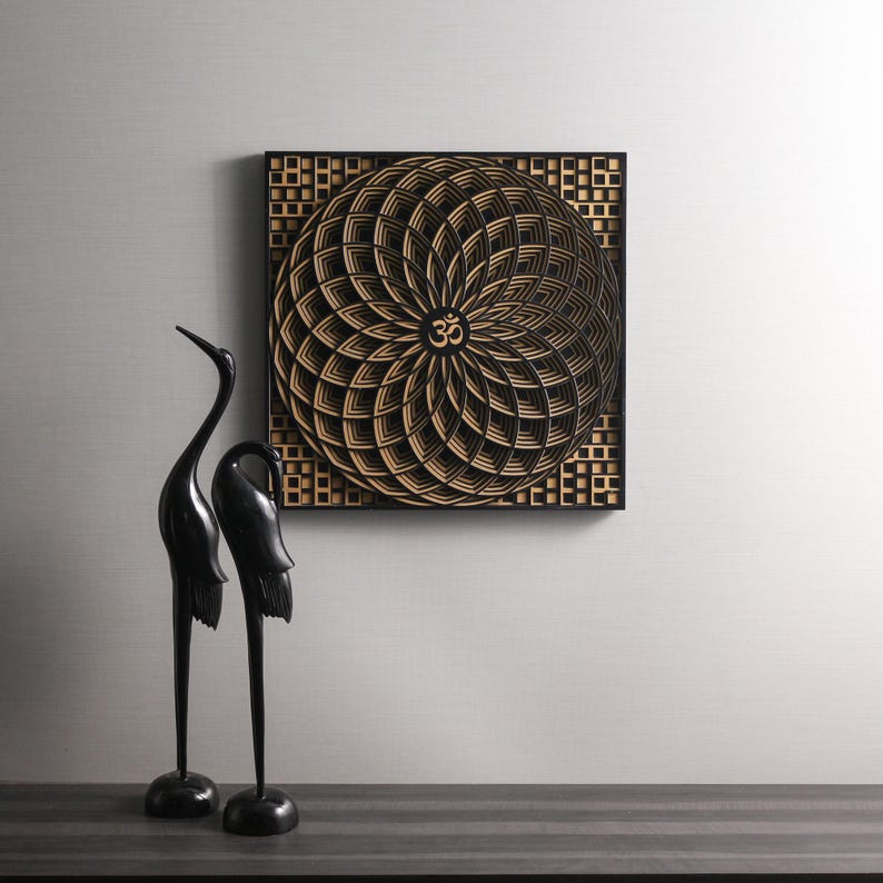 May include: A black square wooden wall art piece with a geometric design in a light wood color. The design features a circular pattern with an Om symbol in the center. Two black bird sculptures are in the foreground.