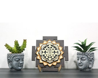 May include: A wooden wall hanging featuring a Sri Yantra mandala in shades of brown and gold. The mandala is surrounded by a decorative border and is mounted on a stand.