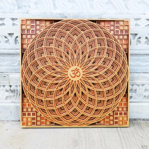 May include: A wooden wall art piece with a mandala design featuring a layered, geometric pattern in shades of brown and orange. The center of the mandala features the symbol "Om" in a gold color.