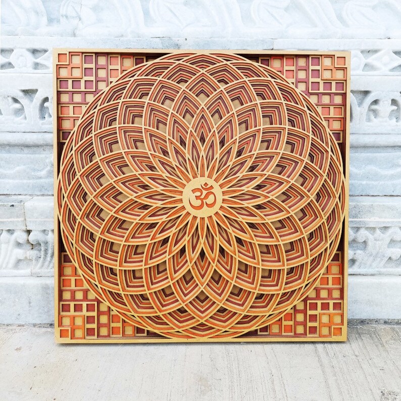 May include: A wooden wall art piece with a mandala design featuring a layered, geometric pattern in shades of brown and orange. The center of the mandala features the symbol "Om" in a gold color.