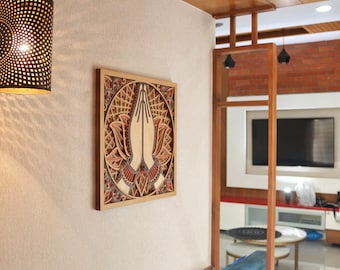 May include: A wooden wall art piece with a carved design of two hands in a prayer position, surrounded by a lotus flower pattern. The hands are painted a light brown color, and the lotus flower is painted in shades of red and brown.