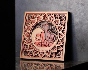 May include: A wooden wall art piece with a mandala design and a layered, 3D effect. The mandala is in shades of brown and red, and features a yin yang symbol with two figures in a meditative pose.