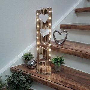 Könnte beinhalten: Eine hölzerne Herz-Leuchte mit einer Lichterkette. Die Leuchte ist aus recyceltem Holz gefertigt und hat einen rustikalen Look. Sie steht auf einer Treppe.