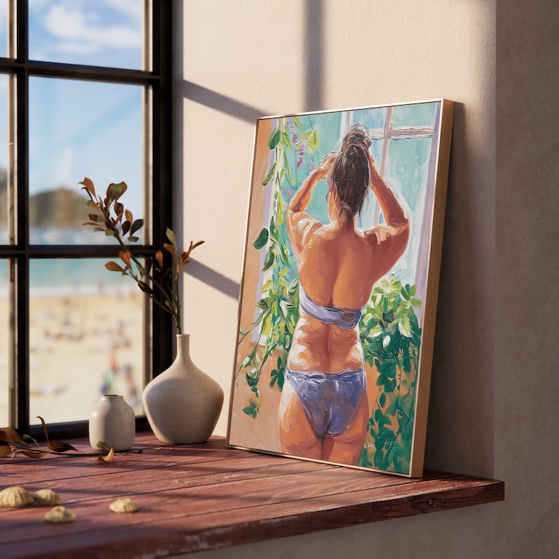May include: A painting of a person standing in front of a window with green plants. The person is wearing a blue bikini top and a blue bikini bottom. The painting is framed in a light wood frame.