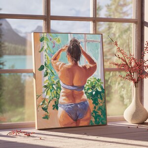 May include: A painting of a person standing in front of a window, looking out at a view of a lake and mountains. The person is wearing a blue bikini top and a blue bikini bottom. The person has their back to the viewer and is adjusting their hair. The painting is framed in a wooden frame.