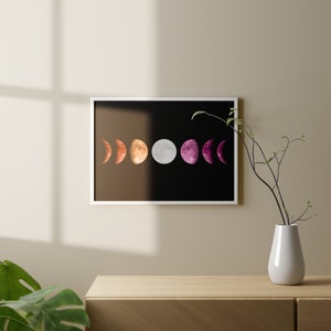 May include: A framed print of a black background with a series of six moons in different phases, colored in a lesbian pride flag color scheme. The moons are in a row from left to right, starting with a crescent moon in red, then a half moon in orange, a full moon in white, a half moon in pink, and a crescent moon in purple.