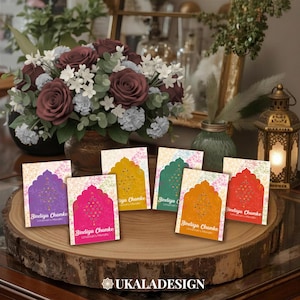 May include: A selection of colourful cards with an arched design and the text "Bindiya Chamke" on a wooden slab. The cards are in shades of purple, pink, yellow, green, and orange. A floral arrangement and decorative lantern are in the background.