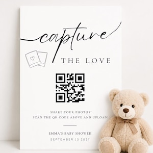 May include: A white rectangular sign with black text reading capture THE LOVE, featuring a QR code, two polaroid icons, and the text SHARE YOUR PHOTOS! SCAN THE QR CODE ABOVE AND UPLOAD! EMMA'S BABY SHOWER SEPTEMBER 15 2027, next to a beige teddy bear.