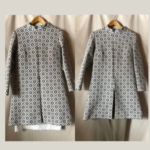 May include: A white, brown, and black patterned coat with a high collar and long sleeves. The coat has a slight A-line shape and a center front slit.