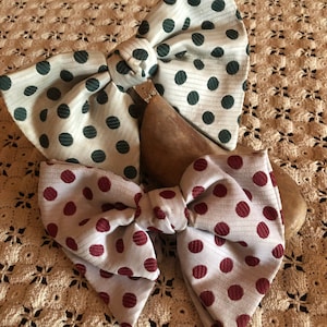 May include: Two fabric bows with polka dots. The top bow is white with dark green polka dots. The bottom bow is white with burgundy polka dots.
