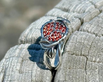 May include: A silver ring featuring a red gemstone set in a leaf design.