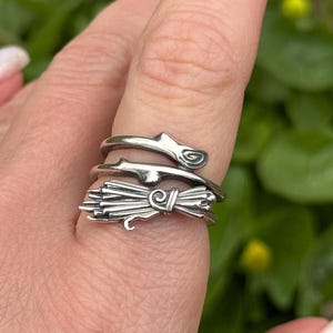 May include: A silver ring featuring a wheat sheaf design. The ring is worn on a finger with other silver rings.