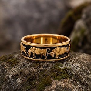 May include: A gold-toned ring featuring a black band inlay with a repeating embossed pattern of golden bulls. The ring has a polished gold interior and edges, showcasing a detailed relief of the animals encircling the entire outer circumference.