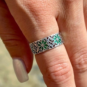 May include: A silver ring with a green and red geometric design. The ring is worn on a finger.