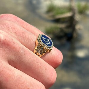 K&ouml;nnte beinhalten: Ein goldener Ring mit einem blauen emaillierten Freimaurer-Symbol. Das Symbol zeigt einen Zirkel und ein Geodreieck mit einem allsehenden Auge in der Mitte.