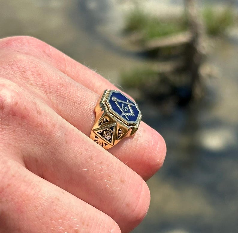 K&ouml;nnte beinhalten: Ein goldener Ring mit einem blauen emaillierten Freimaurer-Symbol. Das Symbol zeigt einen Zirkel und ein Geodreieck mit einem allsehenden Auge in der Mitte.