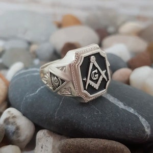 K&ouml;nnte beinhalten: Ein silberner Freimaurer-Ring mit einem schwarzen Emaille-Quadrat und Kompass-Design. Der Ring hat ein silbernes Auge der Vorsehung-Design an der Seite.