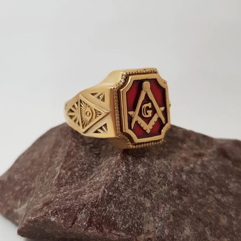 K&ouml;nnte beinhalten: Goldring mit einem roten emaillierten Freimaurer-Symbol, bestehend aus einem Zirkel und einem Winkelma&szlig; mit einem 'G' in der Mitte.