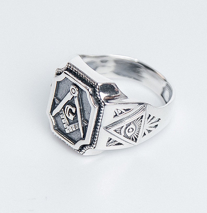 K&ouml;nnte beinhalten: Ein silberner Freimaurer-Ring mit einem Quadrat- und Zirkel-Design und einem allsehenden Auge auf dem Band.