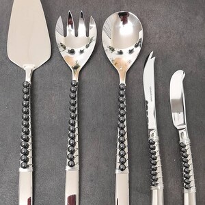 May include: Set of five silver serving utensils with black bead accents. The set includes a cake server, a salad fork, a serving spoon, and two butter knives.