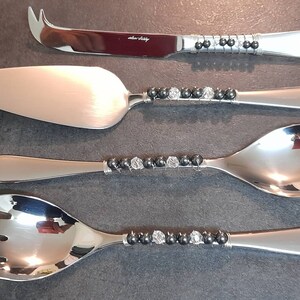 May include: Set of four silver serving utensils with black and clear bead accents. The utensils include a cheese knife, a cake server, a serving spoon, and a serving fork.