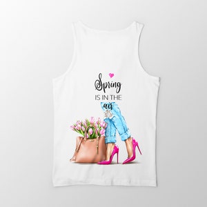 May include: White tank top with a graphic of a woman wearing blue jeans and pink heels holding a brown handbag with pink flowers. The text "Spring is in the air" is printed on the tank top.