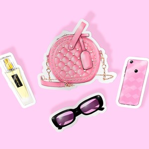 May include: A pink quilted round handbag with a gold chain strap, a pink and white patterned phone case, a pink and black pair of sunglasses, and a clear glass bottle of perfume with a gold cap and the word "LOVE" on the label.