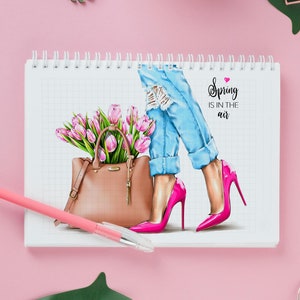 May include: A pink and white gridded notebook with a drawing of a woman wearing blue jeans and pink high heels. She is holding a brown handbag with a bouquet of pink tulips. The text "Spring is in the air" is written on the page.