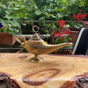 May include: A gold genie lamp with intricate carvings and a crescent moon and star finial. The lamp is sitting on a wooden surface.