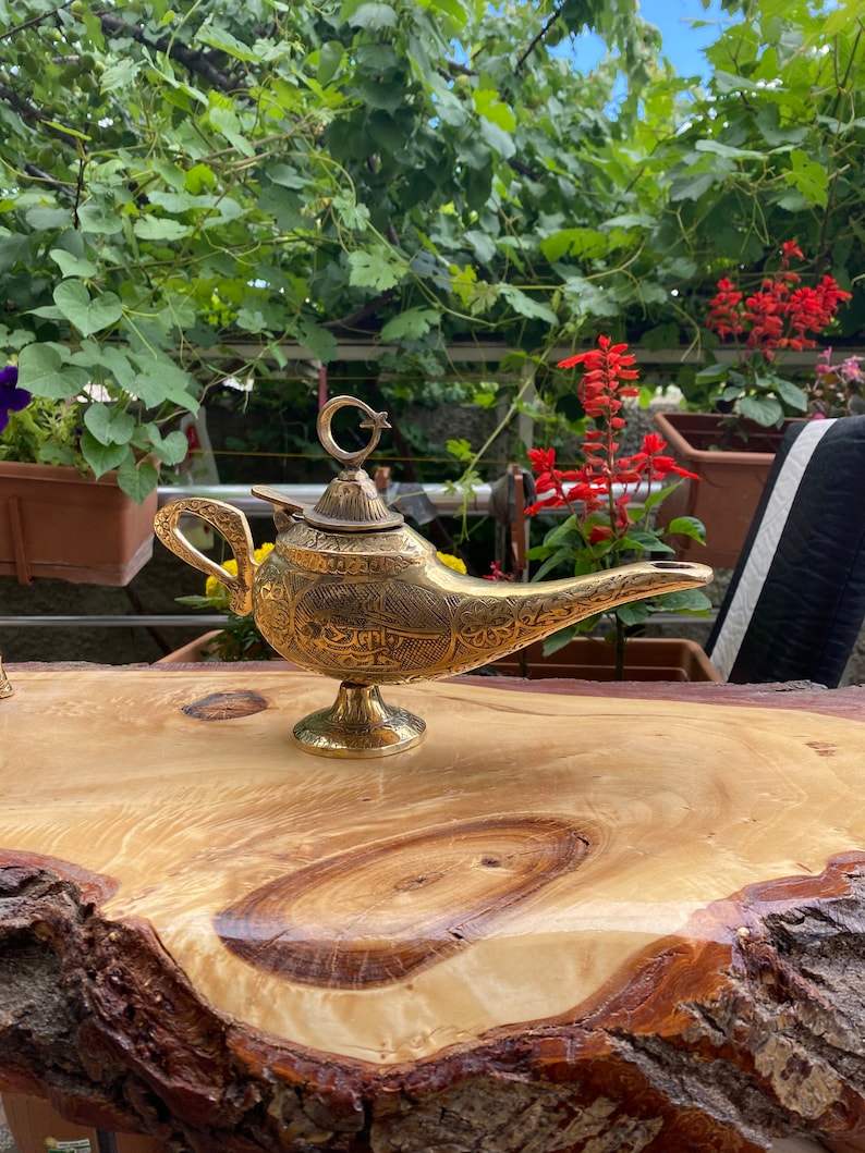 May include: A gold genie lamp with intricate carvings and a crescent moon and star finial. The lamp is sitting on a wooden surface.