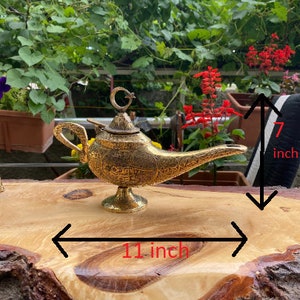 May include: A gold metal genie lamp with intricate details, measuring 7 inches tall and 11 inches wide.