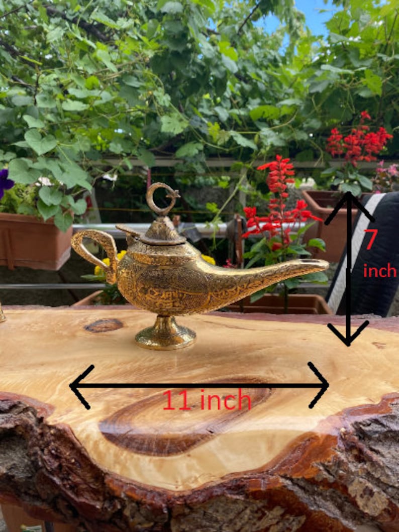 May include: A gold metal genie lamp with intricate details, measuring 7 inches tall and 11 inches wide.