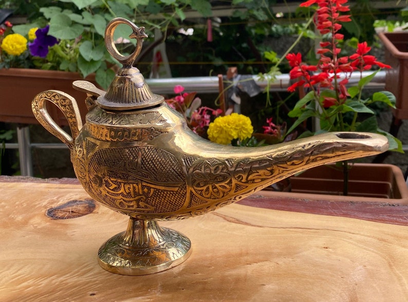 May include: A gold genie lamp with intricate engraved designs and a star and crescent moon finial. The lamp is on a wooden surface.