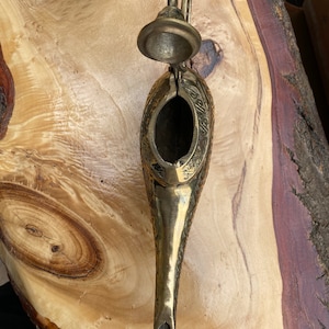 May include: A gold metal genie lamp with intricate details and an open lid. The lamp is on a wooden surface.