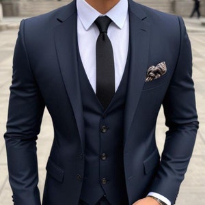 May include: A navy blue three-piece suit with a black tie and a patterned pocket square. The suit jacket has a single button closure and a notched lapel. The vest has a five-button closure. The pants have a flat front.