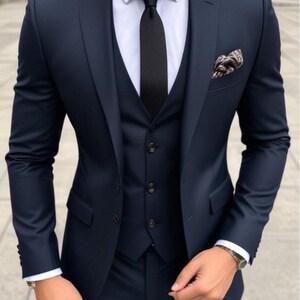 May include: A navy blue three-piece suit with a black tie and a patterned pocket square.  The suit jacket has a single button closure and a notched lapel.  The vest has a five-button closure.  The pants have a flat front and a straight leg.