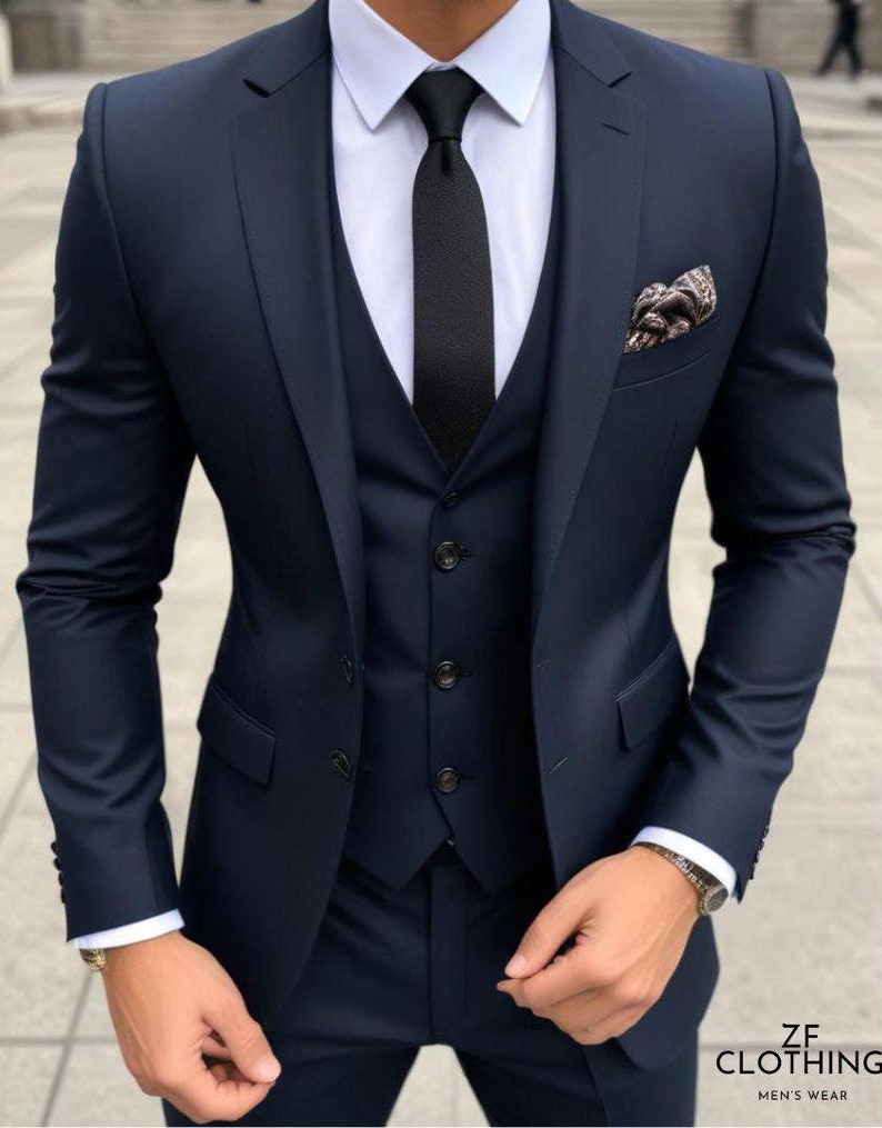 May include: A navy blue three-piece suit with a black tie and a patterned pocket square. The suit jacket has a single button closure and a notched lapel. The vest has a five-button closure. The pants have a flat front.