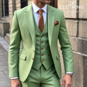 Pu&ograve; includere: Un abito tre pezzi di colore verde chiaro con un gilet e una cravatta marroni. La giacca del vestito ha un fazzoletto da taschino marrone. Il testo "ZF CLOTHING MEN'S WEAR" &egrave; visibile nell'angolo in alto a destra dell'immagine.