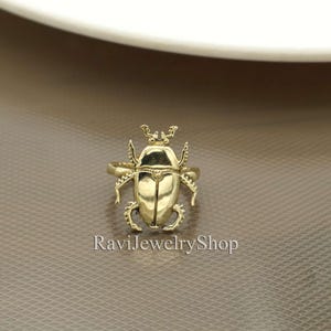 Könnte beinhalten: Ein goldfarbener Ring mit einem detaillierten Käferdesign. Der Ring ist ein Statement-Piece mit einem einzigartigen und auffälligen Design.