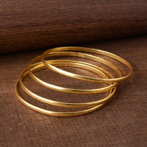 Può includere: Set di quattro braccialetti in metallo dorato. I braccialetti sono impilati uno sopra l'altro.
