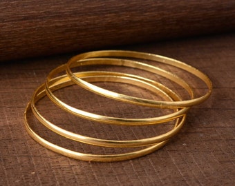 May include: Set of four gold-toned metal bangles. The bangles are stacked on top of each other.