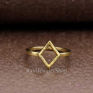 Può includere: Un anello dorato con un design geometrico a forma di diamante. L'anello è in metallo e ha uno stile semplice e moderno.