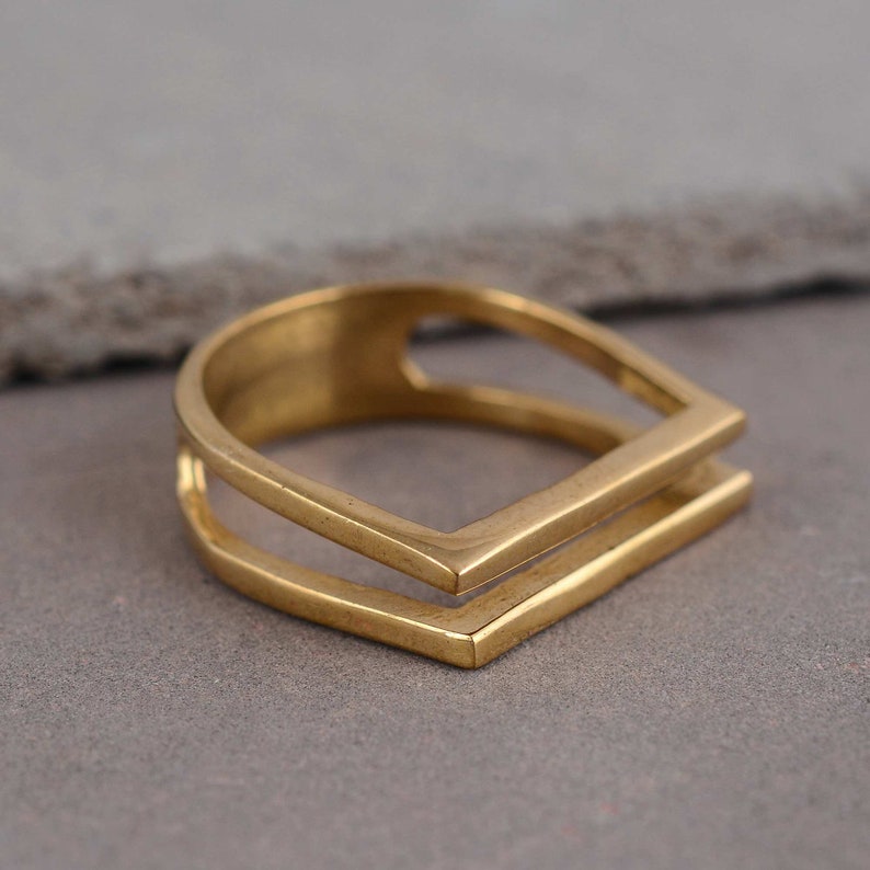 May include: A gold-toned ring with a double-layered square design. The ring is made of metal and has a simple, modern style.