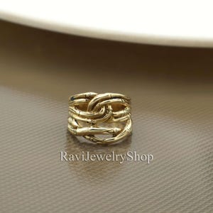May include: A gold-toned ring with a woven bamboo design. The ring is wide and has a textured surface.