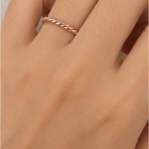 May include: A rose gold ring featuring a twisted rope design. The band has a polished, metallic finish with a continuous spiral pattern that wraps around the entire circumference of the ring, creating a textured appearance on the surface.