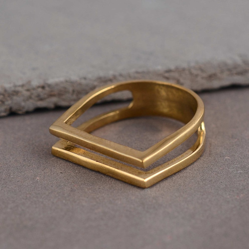 May include: A gold-toned ring with a double square design. The ring is made of metal and has a simple, modern style.