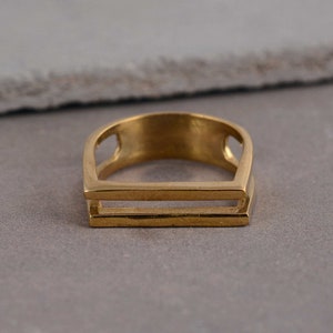 May include: A gold-toned ring with a double-bar design. The ring is made of metal and has a smooth, polished finish.
